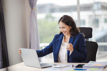 happy young woman excited at work Successful Asian businesswoman with laptop smartphone at work.