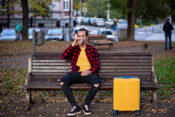Tourist with a rolling suitcase drinking coffee in a park
