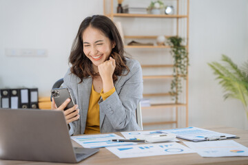 Happy Asian woman holding a smartphone, happy smiling, getting bonus money.