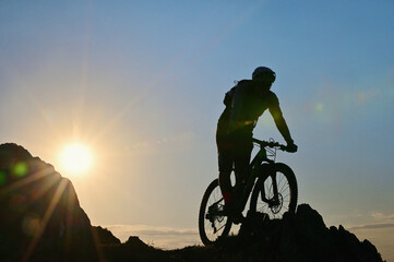 Fototapeta na wymiar Silhouette Of A Cyclist Standing on Clif Against The Sun