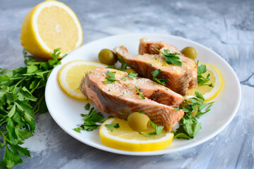 A plate of salmon with lemon slices and olives on a marble table  