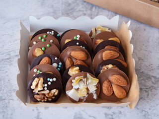 Round chocolate sweets with nuts (mediants) in a box. Side view. Light background.