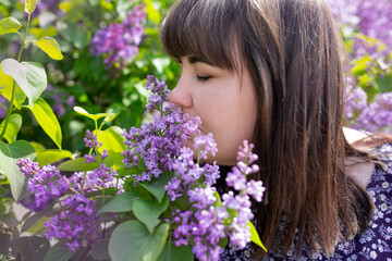 Portrait of an attractive woman surrounded by lilac bushes. Spring and summer, seasonal photos. Vertical photo.