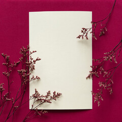 Summer, autumn wedding, birthday, holiday. Closeup of empty greeting card, invitation mockup with blank beige sheet of paper and decorative red dry flowers. Basic textile red background.