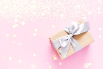  Flatlay of festive craft gift boxe in wrapping paper decorated with silver satin ribbon bows over pink background with stars, top view, horizontal composition. Christmas or birthday day boxing concep