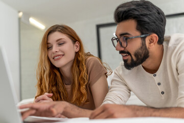 Couple enjoy leisure time at home using laptop computer laying on bed surfing internet together.