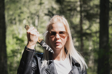 A beautiful girl holds a folding knife in her hand in the forest.