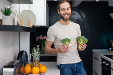 Obraz premium Man holding green fresh broccoli standing in modern kitchen at home.
