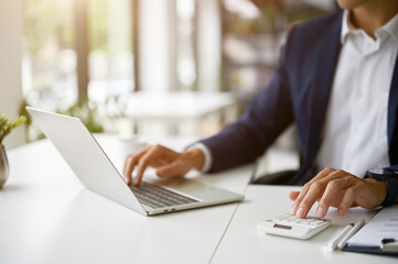 Close-up image of a professional Asian businessman using a laptop and calculator