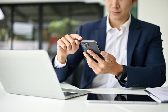 Close-up image of a smart Asian businessman using his smartphone at his desk.