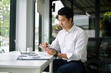 Smart Asian businessman or male boss using his digital tablet at his desk in the office.