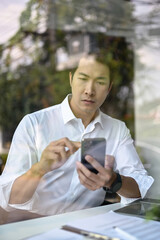 Fototapeta premium Portrait of a focused Asian businessman checking his messages on his smartphone