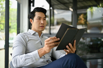 Smart Asian businessman checking his meeting schedule on a notebook