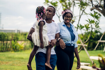 Fototapeta premium Portrait of enjoy happy love black family african american father and mother with little african girl child smiling and play having fun moments good time in park at home