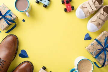 Son congratulates Dad on Father's Day. Overhead view of dad's leather shoes, son's tiny sneakers, hearts, toy cars, mugs of cocoa, and gift boxes on yellow backdrop with empty frame for text or ad