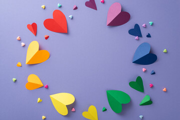 Show your true colors with this top view flat lay of pride-themed items, featuring a rainbow colored paper hearts on a lilac backdrop with an empty circular frame for text or advert