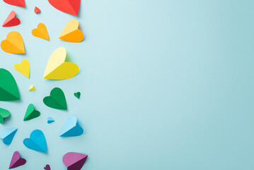 LGBT History Month concept. Top-down shot of symbolic parade accessories, including a rainbow colored paper hearts, laid out on a pastel blue backdrop with space for text - obrazy, fototapety, plakaty