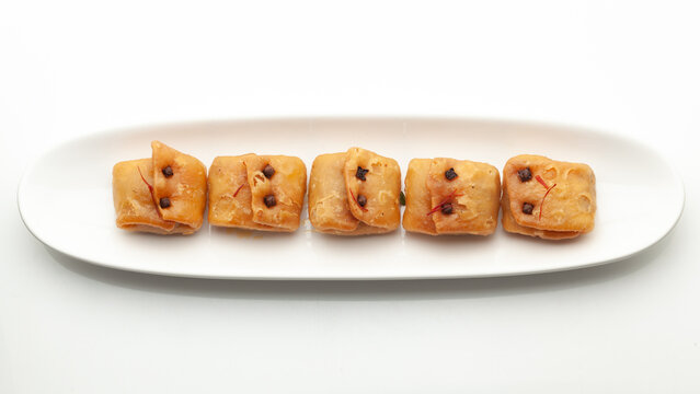 Assorted Indian Bengali traditional sweet "Labanga Latika" or "Lavang Latika", on an oval white ceramic plate. Top view. Isolated on white.