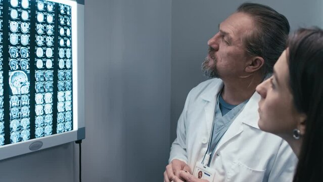 Professional medical workers reading patients X-ray image placed on lightbox and discussing plan of surgery