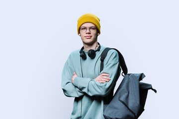 Young male in yellow cap sweatshirt with headphones backpack on white background