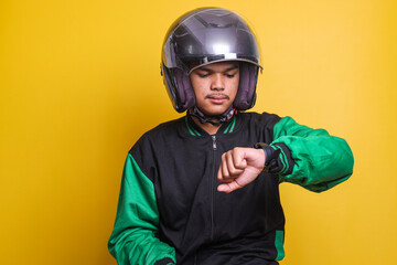 Asian online taxi driver wearing green jacket and helmet checking the time on wrist watch isolated...