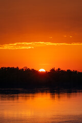 Golden sunset and sunset with clouds over forest and river or lake