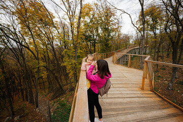 Mother with baby girl daughter in hands looking at wild animals from wooden bridge.