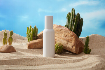 White bottle without label decorated with some stones and green Cacti on the beach sand. Branding...