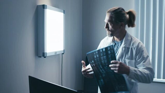 Mature Caucasian doctor with long hair placing brain X-ray image onto lightbox to inspect it
