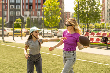 Obraz premium mother, daughter, oval brown leather rugby ball playing american football in park. Family and kids, nature concept.