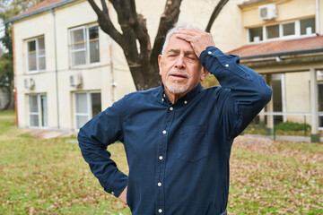 Frustrated elderly man standing in garden of nursing home
