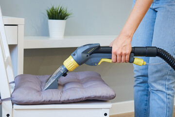 Close-up woman doing furniture dry cleaning with vacuum cleaner in apartment
