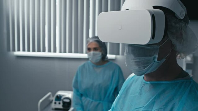 Tilt up of professional surgeon wearing VR headset using modern technology during work with patient in operating theater