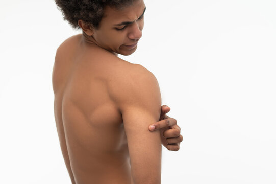 Curly-haired young guy suffering from pain in his shoulder