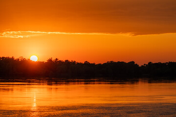 Golden sunset over a river or lake. The Sun goes down to the horizon above the trees