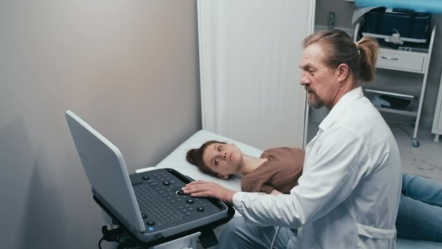 High angle of mature Caucasian doctor doing thyroid ultrasonography for female patient with hypothyroidism
