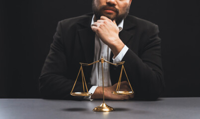 Lawyer in a black suit sits attentively on his office desk with a golden scale balance, symbol of legal justice and integrity, balanced and ethical decision making in the court of law. equility - obrazy, fototapety, plakaty