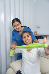 Fototapeta premium Concept of World Confederation for Physical Therapy. young physiotherapist caregiver helping mature elderly woman training with elastics in rehabilitation center, muscle weakness