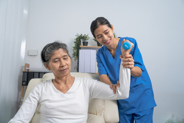Fototapeta premium Young pretty asian physiotherapist helping senior female patient holding dumbbell in physical therapy session, concept of World Confederation for Physical Therapy.