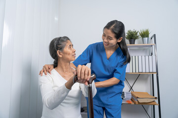 Attentive practitioner nurse assisting physical therapy elderly woman on a walking wood standard cane in disability nursing rehabilitation center, physical therapy encourage hands.