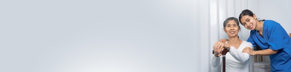 Fototapeta premium Attentive practitioner nurse assisting physical therapy elderly woman on a walking wood standard cane in disability nursing rehabilitation center, physical therapy encourage hands.