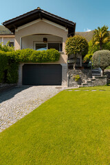 Exterior of a small detached house with a nice green garden and garage. Sunny spring day