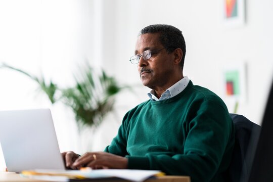 Concentrated Ethiopian male entrepreneur with laptop looking at screen and analyzing data while sitting at desk and working on project in spacious workplace