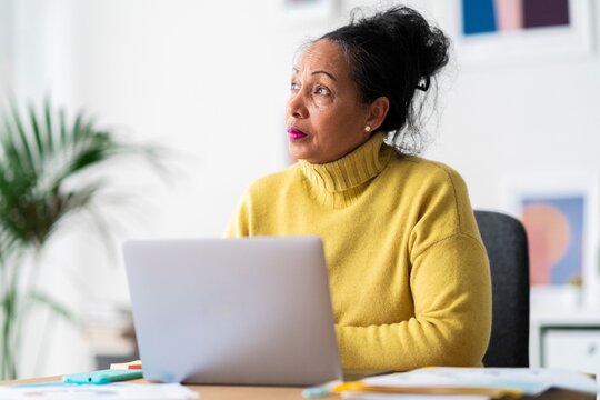 Focused senior Ethiopian female office worker looking away and contemplating while creating business strategy and working online on wireless laptop