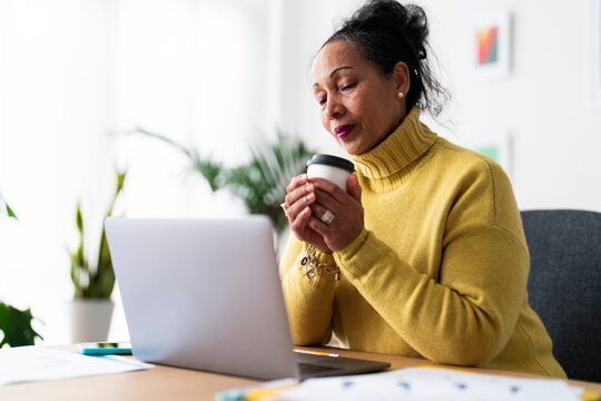 Ethiopian female entrepreneur with cup of hot drink analyzing strategy of startup project while working at desk on portable laptop