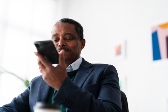 adult Ethiopian male CEO director in formal suit making conversation on mobile phone recording voice message while working in office