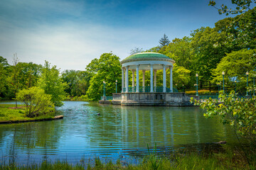 Obraz premium Bandstand Pavilion and water fountain on the Roosevelt Lake and woodland at Roger Williams Park, Providence, Rhode Island