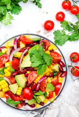 Spicy salad with sweet corn, red beans, avocado, jalapeno, cherry tomatoes, red onion and cilantro. White table background, top view