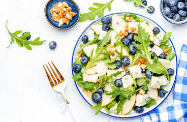 Gourmet summer salad with sweet pears, blueberries, blue cheese, arugula and walnuts. White kitchen...