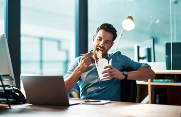 Business, man and eating noodles in office at desk, laptop and working in startup company at night. Hungry young male employee, fast food and late dinner at computer technology in agency at evening